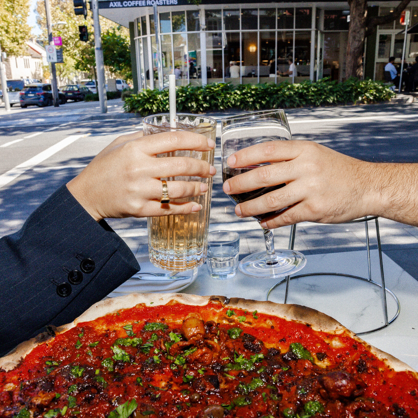 wo people clinking drinks over a freshly baked pizza at an outdoor table at 170 Grammi.