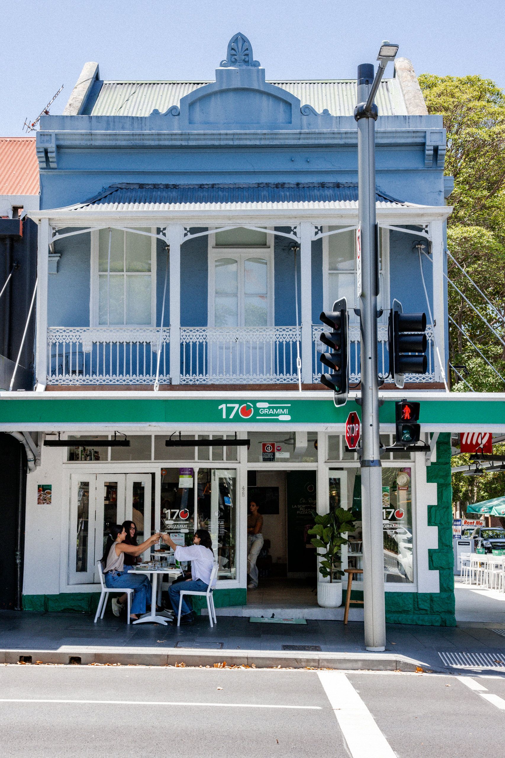 Exterior of 170 Grammi in Surry Hills, a blue heritage-style building with green signage and outdoor seating on a sunny street corner.