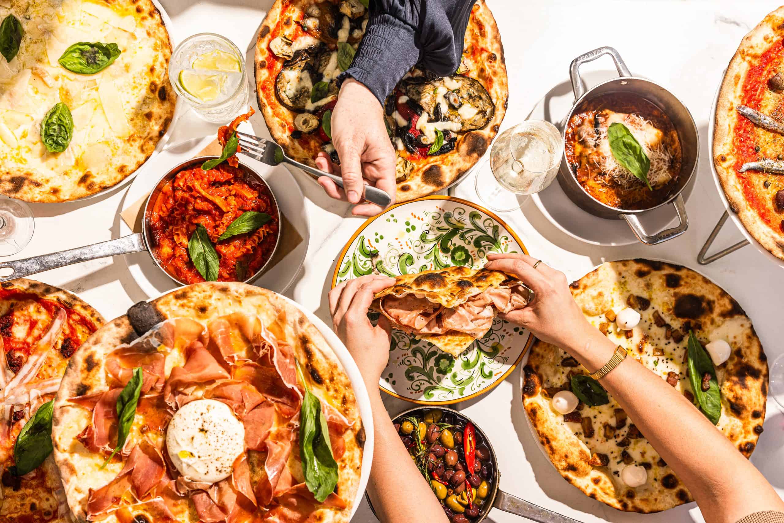 Overhead view of diners sharing Italian pizzas, antipasti, and schiacciata with mortadella at 170 Grammi in Sydney