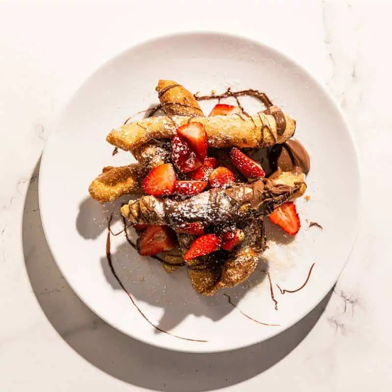 Lightly fried Italian dough sticks drizzled with Nutella and topped with fresh strawberries, a sweet and indulgent treat