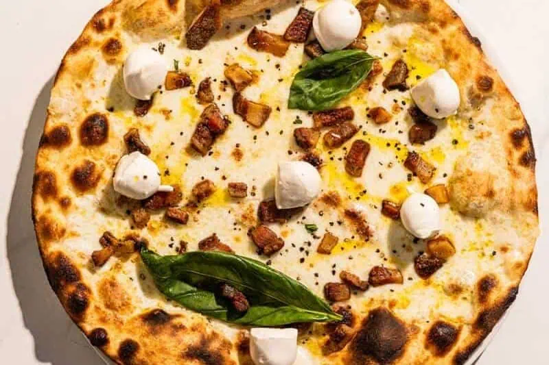 Bufalina pizza with a white base, topped with guanciale, buffalo mozzarella, black pepper, basil, and Coratina EVOO