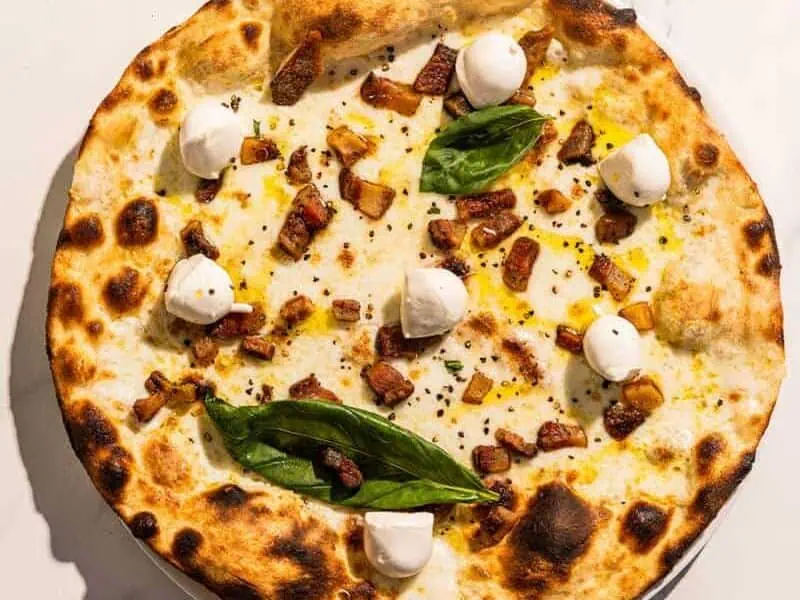 Bufalina pizza with a white base, topped with guanciale, buffalo mozzarella, black pepper, basil, and Coratina EVOO