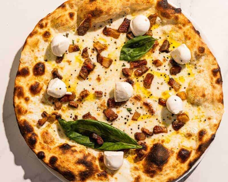 Bufalina pizza with a white base, topped with guanciale, buffalo mozzarella, black pepper, basil, and Coratina EVOO
