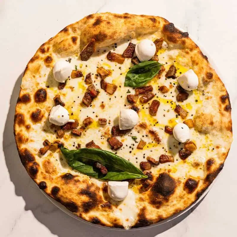 Bufalina pizza with a white base, topped with guanciale, buffalo mozzarella, black pepper, basil, and Coratina EVOO