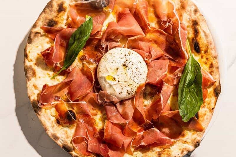 Pizza topped with San Marzano tomato, Levoni Prosciutto San Daniele, La Stella burrata, fresh basil, and Coratina EVOO