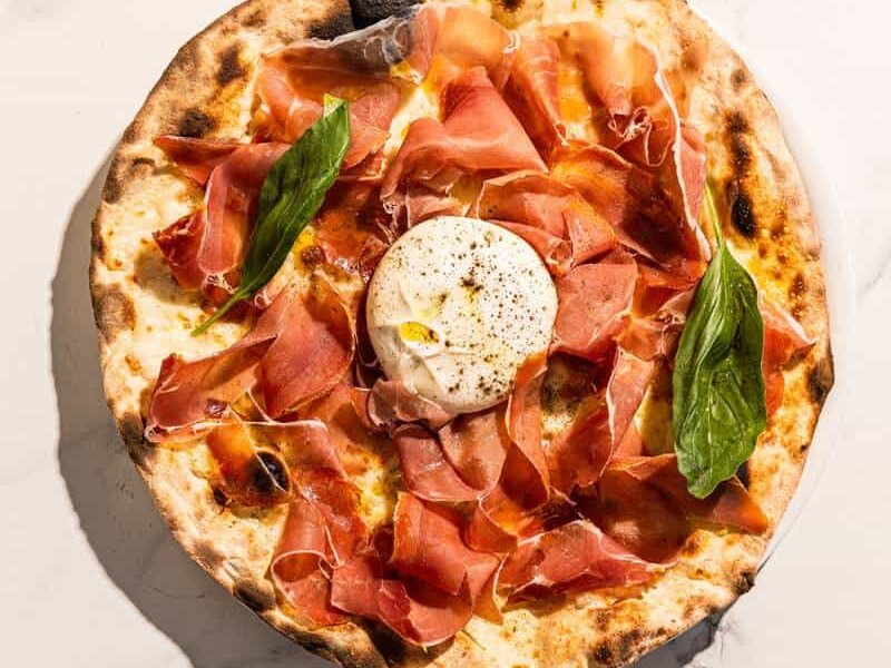 Pizza topped with San Marzano tomato, Levoni Prosciutto San Daniele, La Stella burrata, fresh basil, and Coratina EVOO
