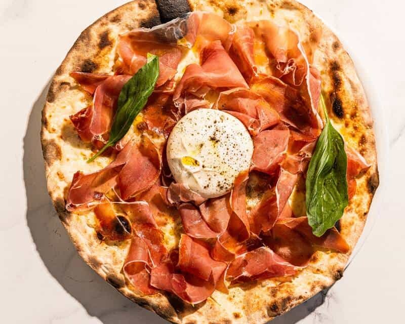Pizza topped with San Marzano tomato, Levoni Prosciutto San Daniele, La Stella burrata, fresh basil, and Coratina EVOO