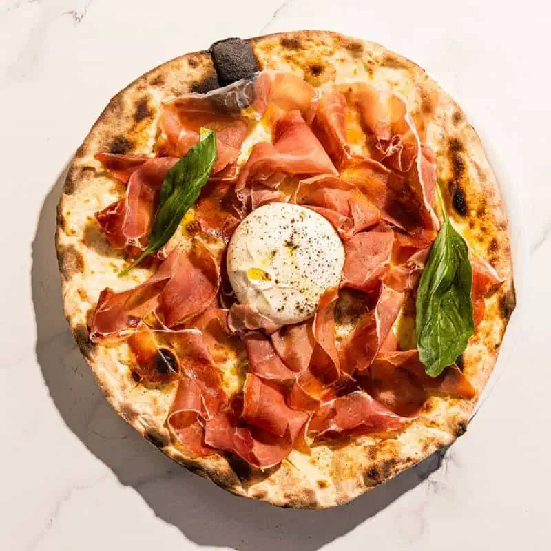 Pizza topped with San Marzano tomato, Levoni Prosciutto San Daniele, La Stella burrata, fresh basil, and Coratina EVOO