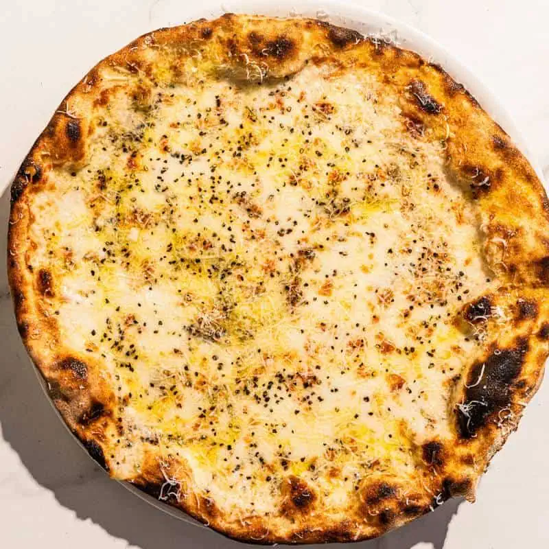 Roman-style Cacio e Pepe pizza with a white base, topped with Pecorino Romano cheese and freshly cracked black pepper