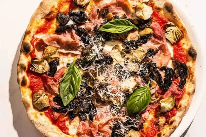 Capricciosa pizza topped with San Marzano tomato, buffalo mozzarella, double smoked ham, sautéed mushrooms, marinated artichokes, and fresh basil
