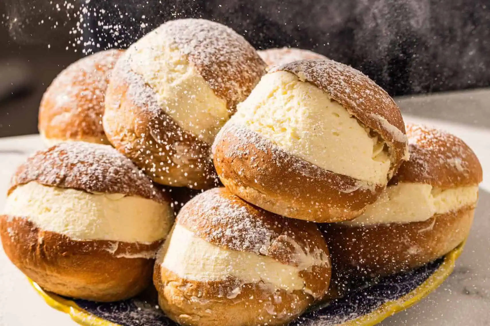Plate of soft maritozzi brioche buns filled with sweet whipped cream, being dusted with powdered sugar at 170 Grammi