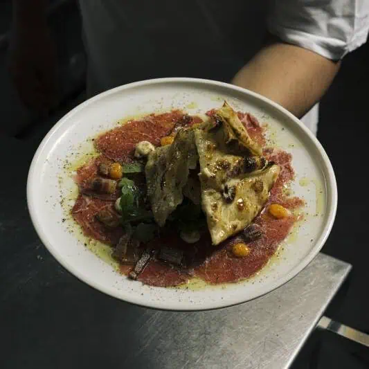 Thinly sliced eye fillet beef carpaccio served with egg yolk, guanciale, Pecorino Romano cream, croccante bianca, and rocket