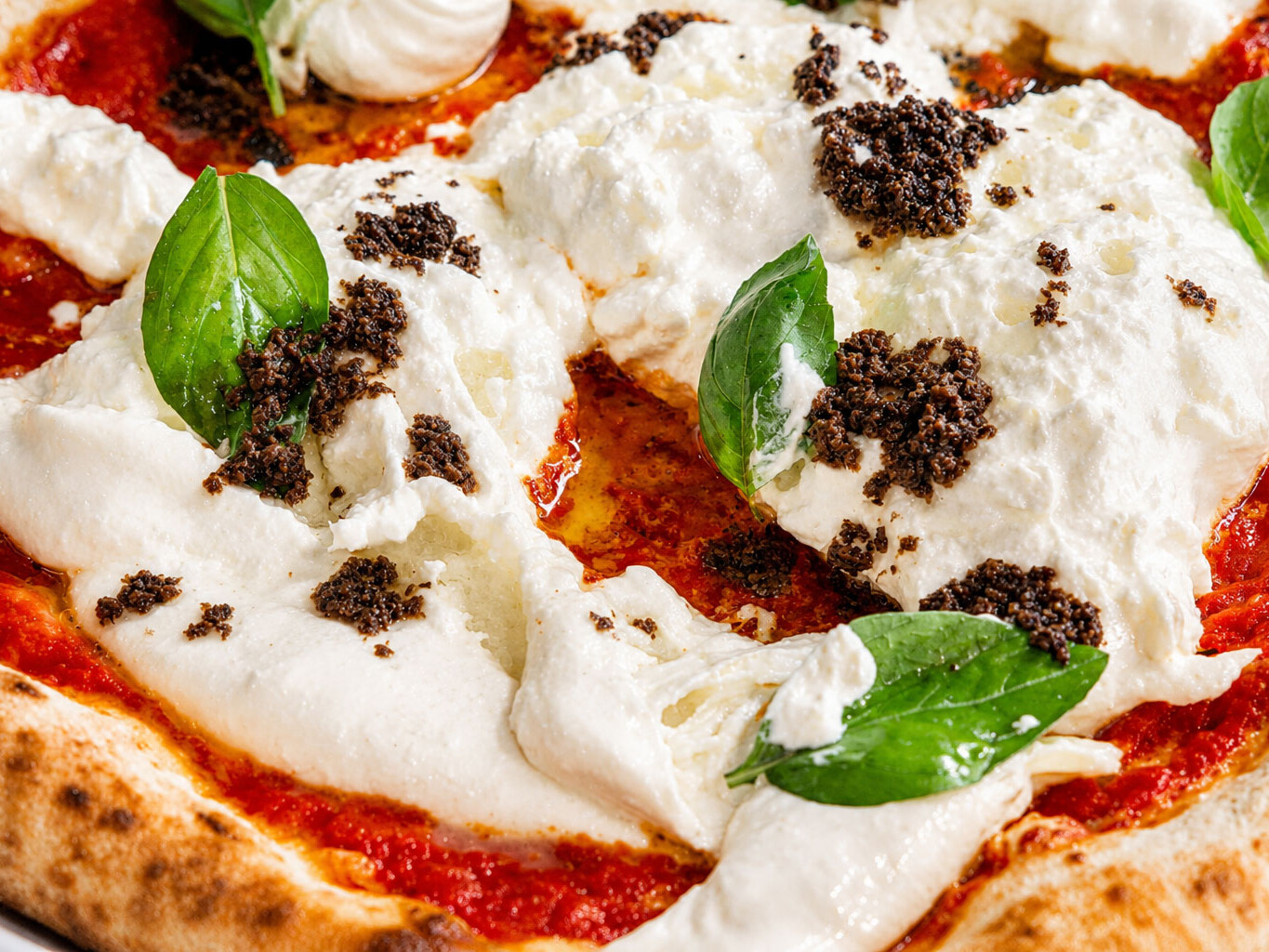 Close-up of a Roman pizza topped with creamy fior di latte, fresh basil leaves, and black truffle.