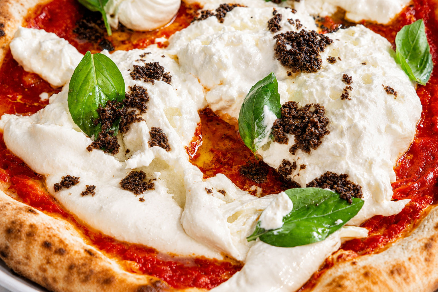 Close-up of a Roman pizza topped with creamy fior di latte, fresh basil leaves, and black truffle.
