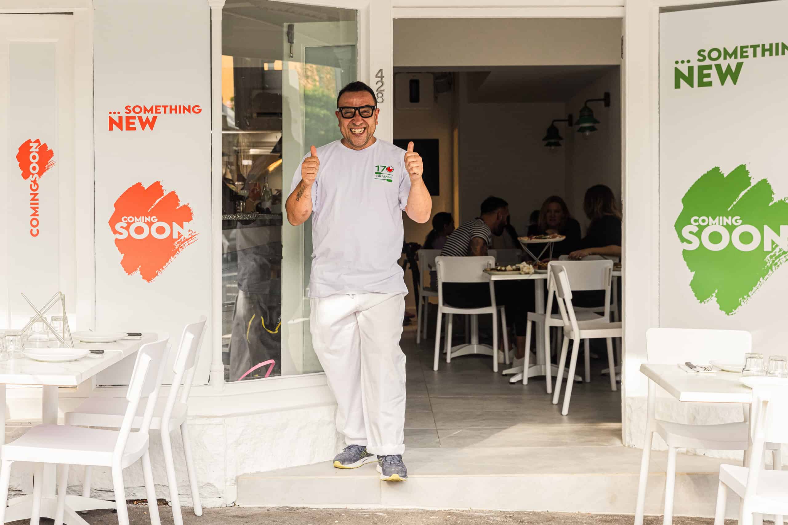 Chef Luigi Esposito giving two thumbs up outside 170 Grammi Pizzeria with “Coming Soon” signs on the windows