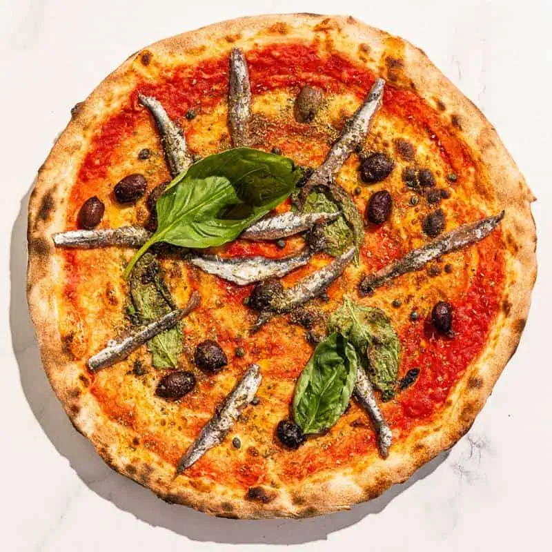 Traditional Napoletana pizza with San Marzano tomato, Cetara anchovies, Sicilian capers, Gaeta black olives, basil, and Coratina EVOO – no cheese