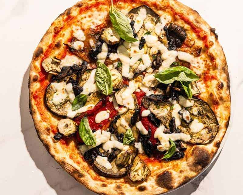 Ortolana pizza topped with San Marzano tomatoes, buffalo mozzarella, sautéed mushrooms, grilled eggplant, capsicum, marinated artichokes, fresh basil, and Coratina EVOO
