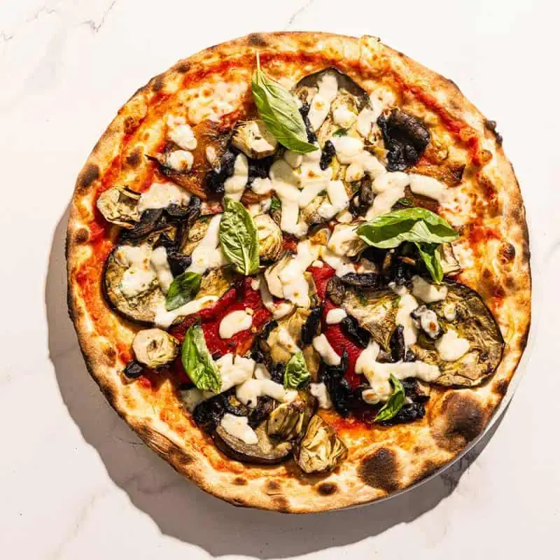 Ortolana pizza topped with San Marzano tomatoes, buffalo mozzarella, sautéed mushrooms, grilled eggplant, capsicum, marinated artichokes, fresh basil, and Coratina EVOO