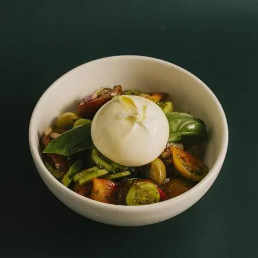 Fresh panzanella salad with heirloom tomatoes, cucumber, green olives, Spanish onions, croutons, creamy burrata, EVOO, oregano, and basil