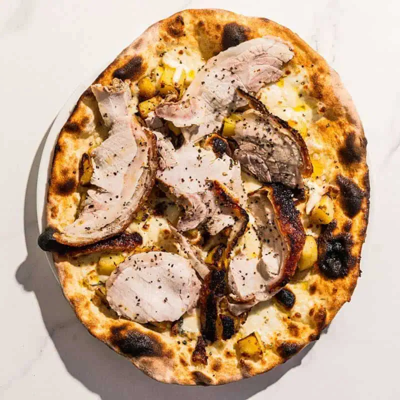 White base pizza topped with Porchetta alla Romana, smoked scamorza, wood-fired roasted potatoes, rosemary, and black pepper