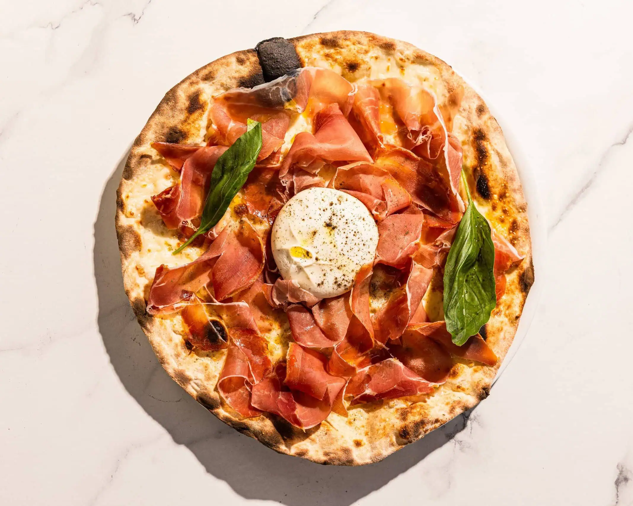 Pizza topped with San Marzano tomato, Levoni Prosciutto San Daniele, La Stella burrata, fresh basil, and Coratina EVOO